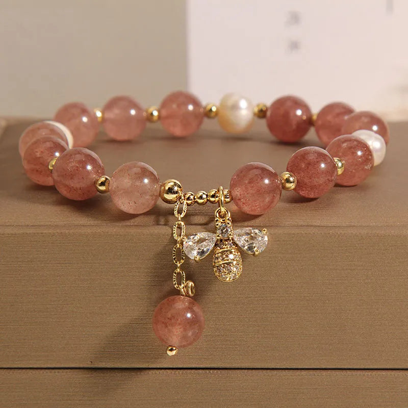 Adjustable pink strawberry quartz bracelet with three freshwater pearls and sparkling zircon charms on a wrist.