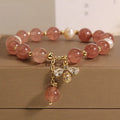 Adjustable pink strawberry quartz bracelet with three freshwater pearls and sparkling zircon charms on a wrist.