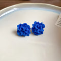 Handmade geometric cloth earrings with a blue resin flower and silver detail on a white background.