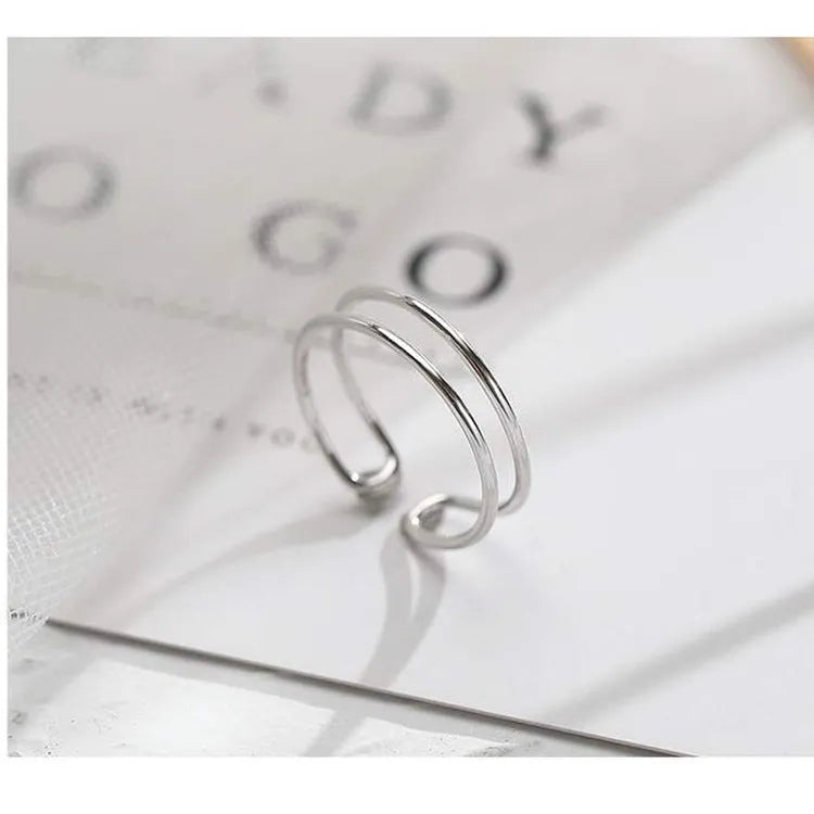 Silver plated geometric cross ring with adjustable opening on a plain background