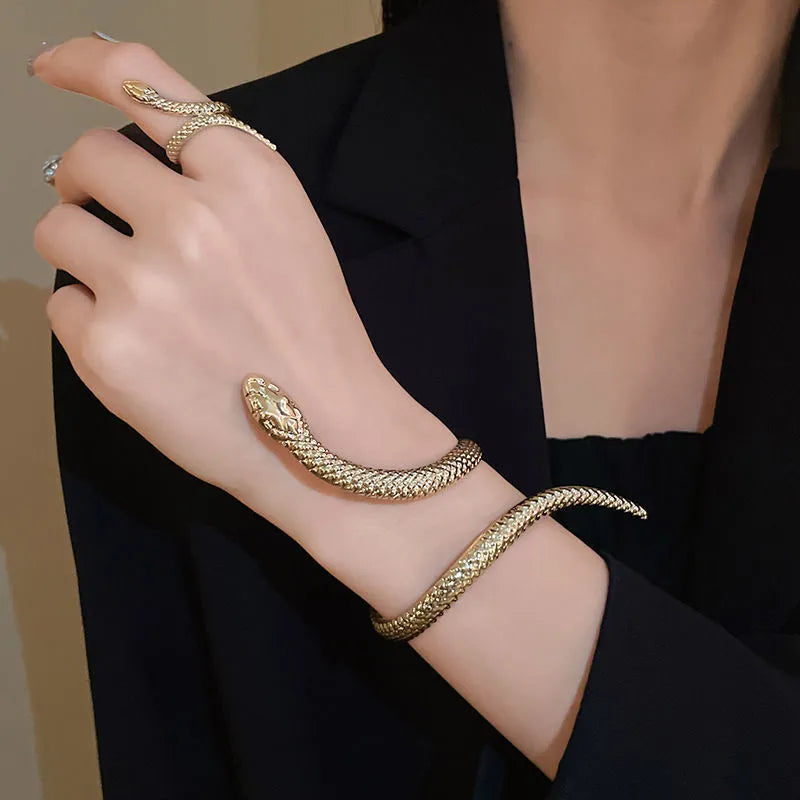 Gold exaggerated twisted snake design bracelet and ring jewellery set on a dark background.