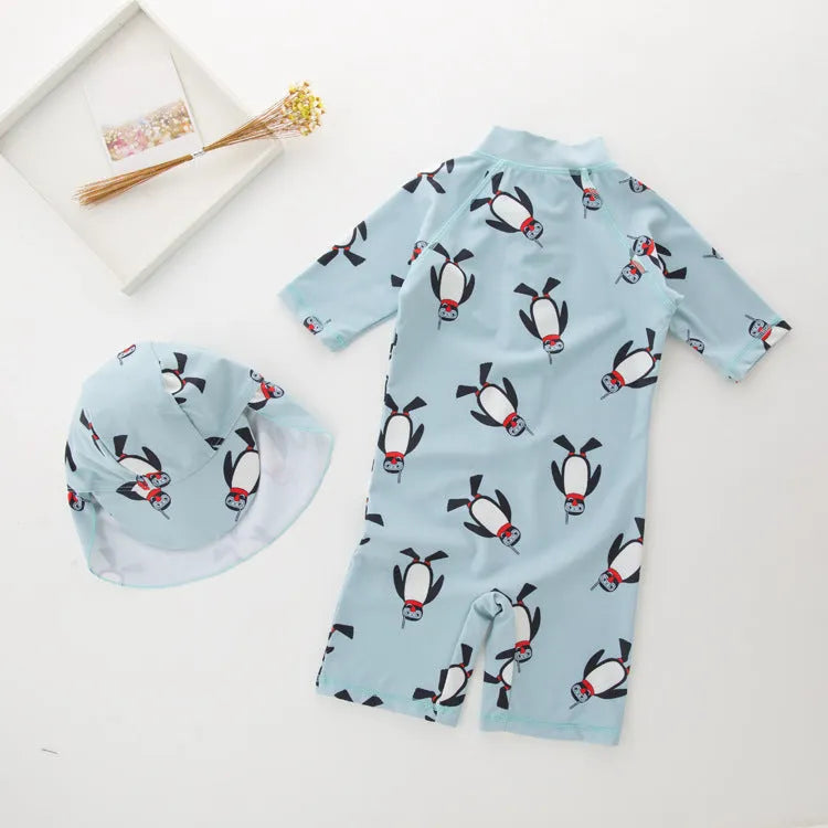 Boys' blue and white penguin print long sleeve swimsuit with matching swimming cap laid flat.