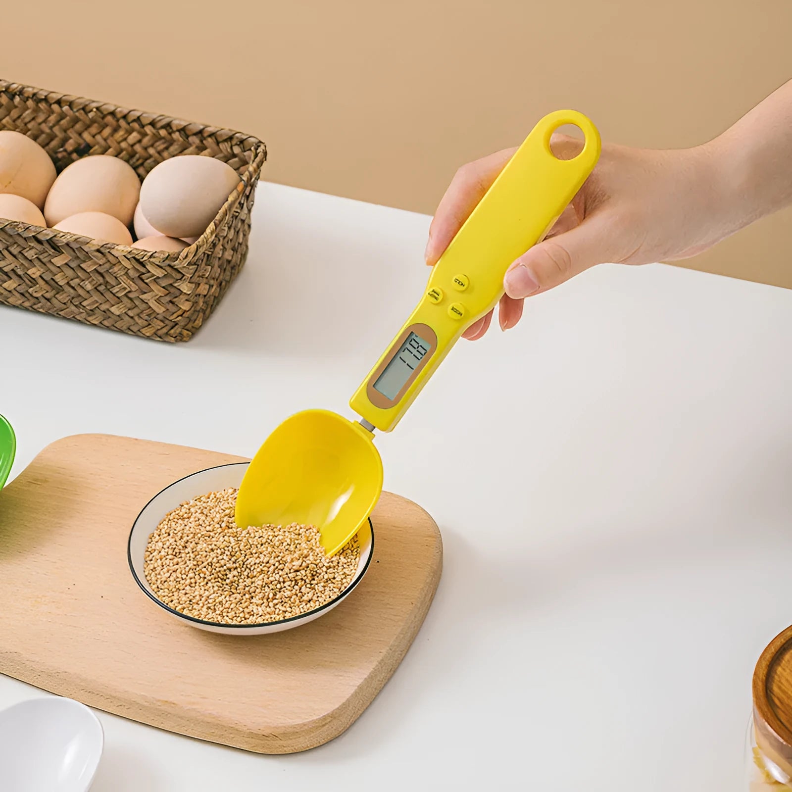 White digital kitchen scale with LCD screen displaying weight, shown next to a measuring spoon.