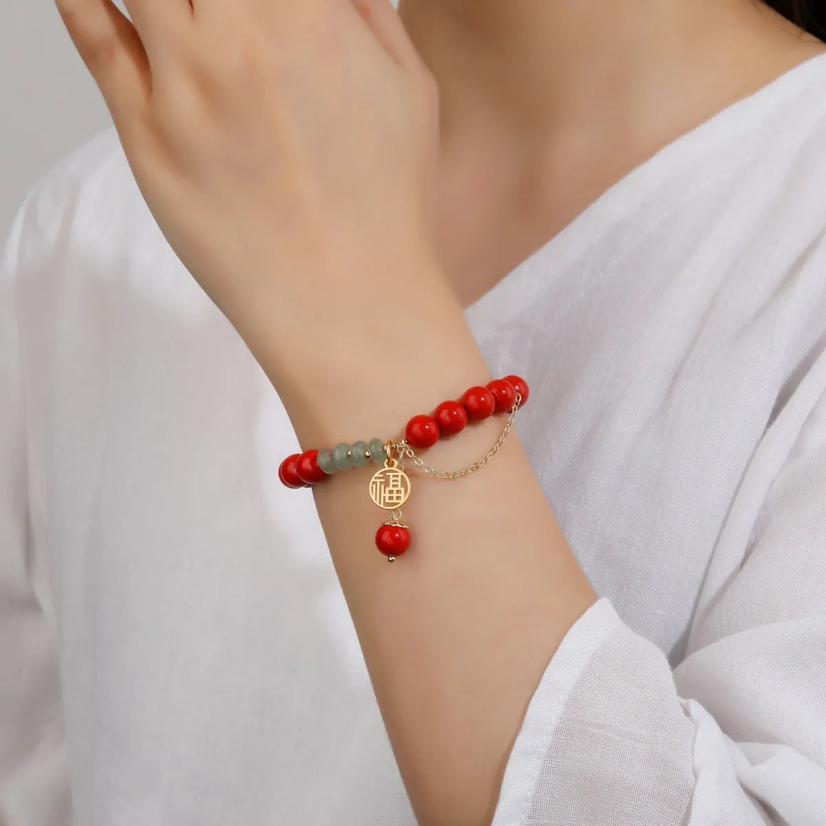 Close-up of a red cinnabar women's bracelet with a Fu character, jade spacer beads, and a small red tassel.