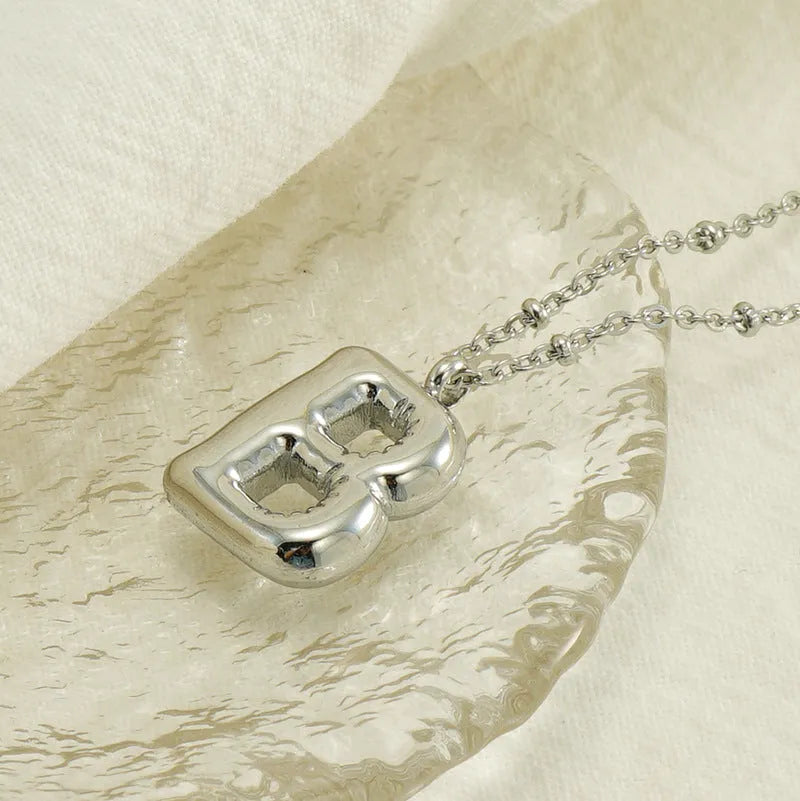 Gold bubble letter N pendant on stainless steel clip beads chain necklace against white background