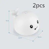 White and blue whale-shaped bath toy spraying water with LED lights on, floating in a baby bath