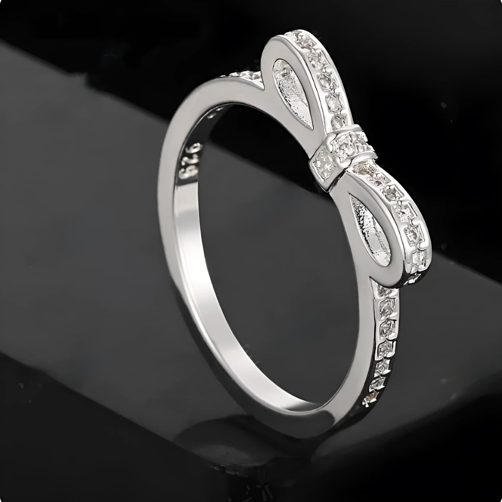 Silver electroplated bow ring with sparkling zircon crystals on a finger.