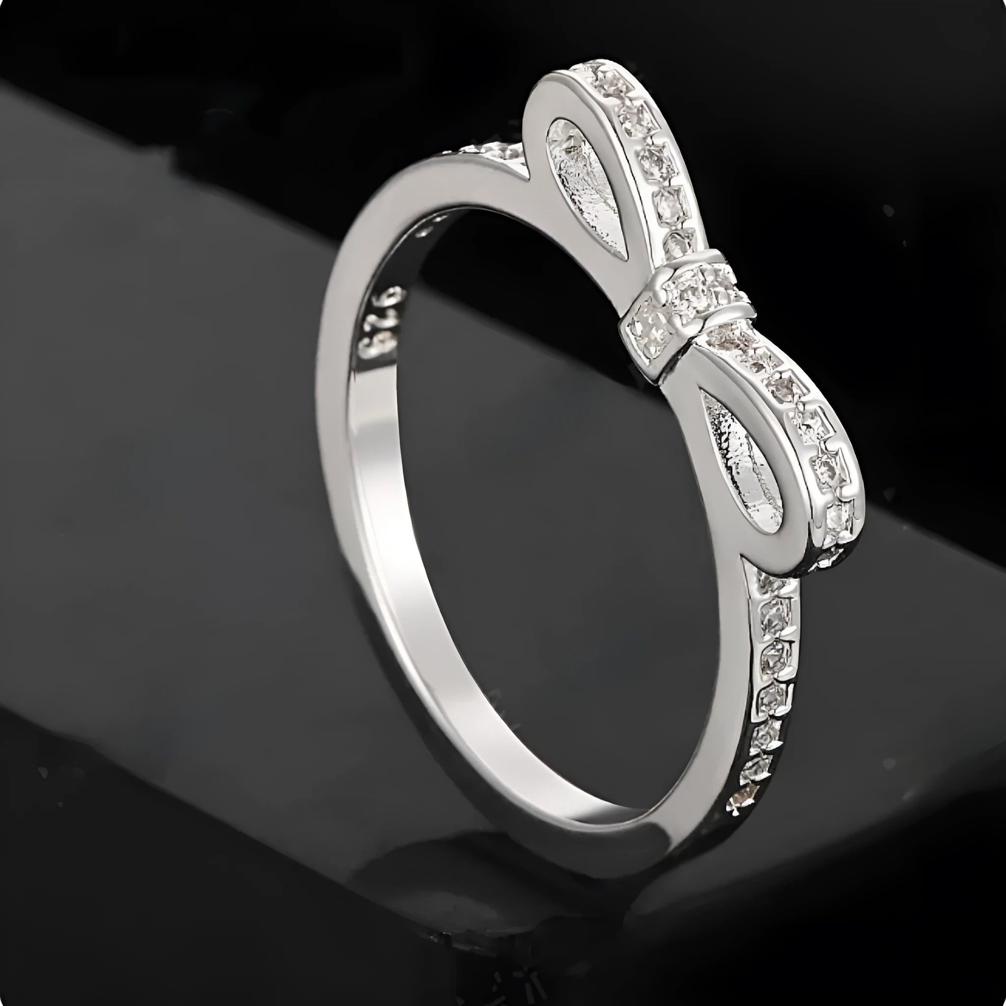 Silver electroplated bow ring with sparkling zircon crystals on a finger.