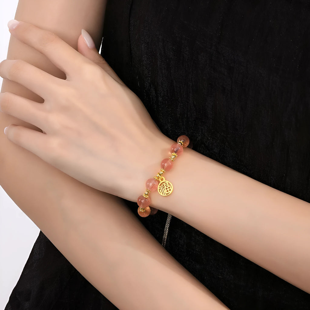 Close-up of a women's adjustable bracelet with pink strawberry quartz crystal beads and a silver fu charm on a geometric chain.