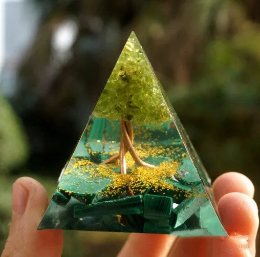 Clear epoxy resin pyramid ornament with natural crystal gravel inside on a wooden surface.