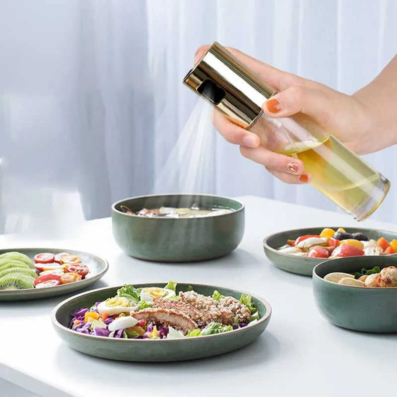 Gold pump-action oil and vinegar spray bottle with 100ml glass body on kitchen counter.