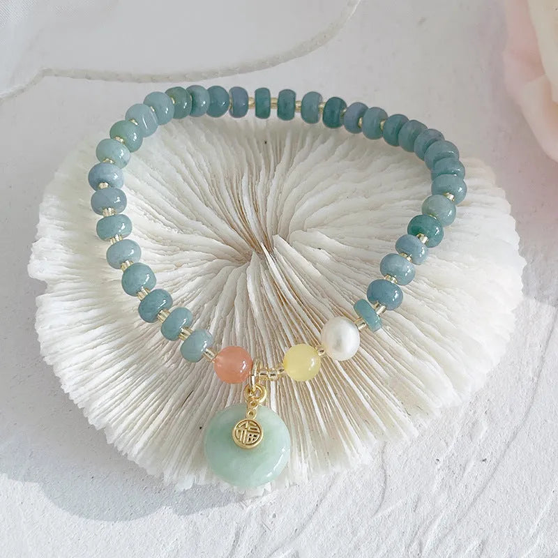 Close-up of a blue jade women's bracelet showing a gourd charm and a peace buckle charm on a string.