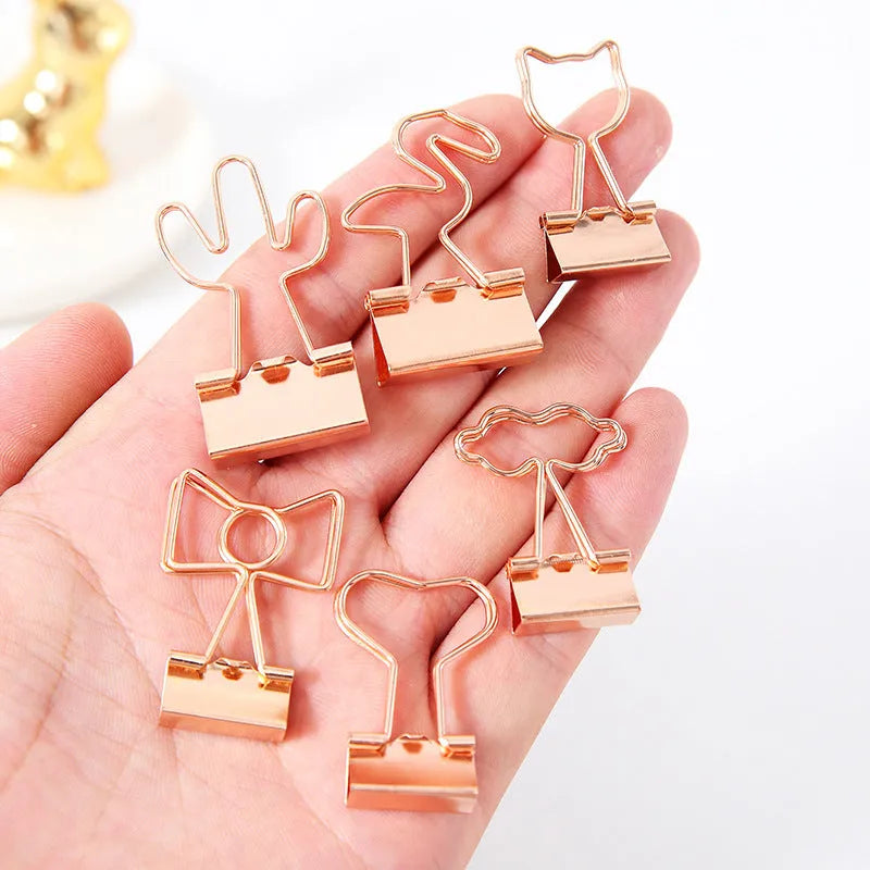 Small gold-plated metal office clip with a long tail, shown in a choice of flamingo, love, clouds, cat, and cactus shapes.