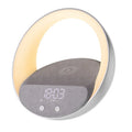 Beige multifunctional wireless charging clock with Bluetooth speaker and warm white LED wake-up light on a wooden table.