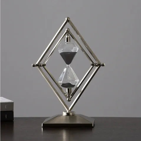 Glass sand clock timer with detailed metal ornaments in a bronze finish, showing modern simplicity style.