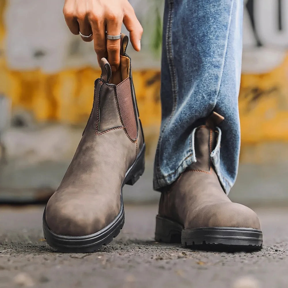 Vintage frosted brown leather Chelsea boots with round toe and car suture detailing on a wooden floor.