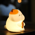 Small yellow Greedy Cat cartoon night light on a desktop, showing fish theme and compact size.