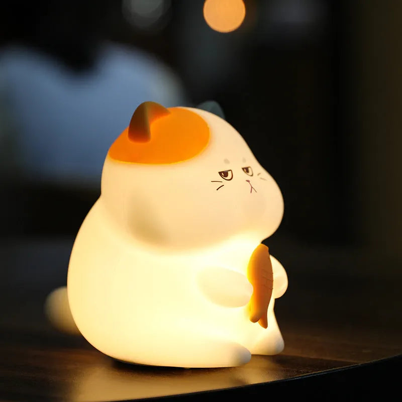Small yellow Greedy Cat cartoon night light on a desktop, showing fish theme and compact size.