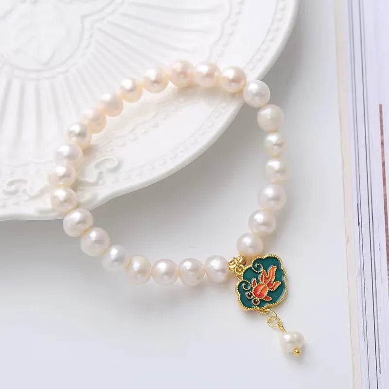 Natural freshwater pearl bracelet with vintage goldfish pendant and lotus motif on white background