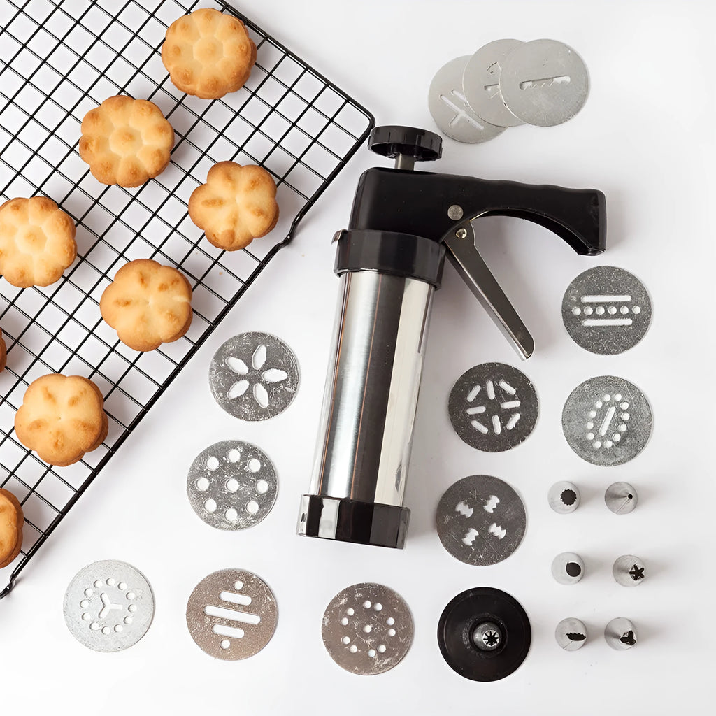Stainless steel biscuit press gun with assorted cookie mould discs and icing nozzles on a baking tray.