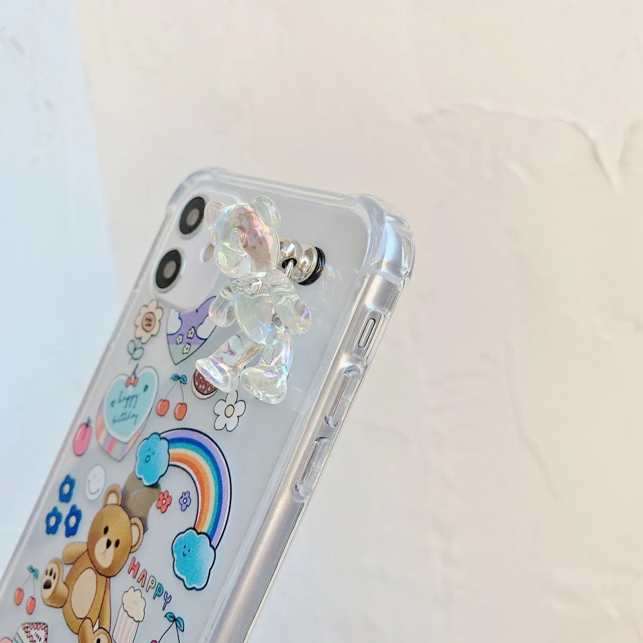 White iPhone case with a bear cartoon design and a silver chain with a bear pendant attached.