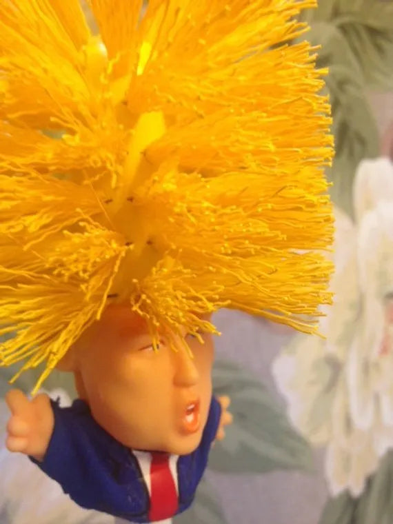 Yellow plastic Donald Trump toilet brush with hanging slot on handle.