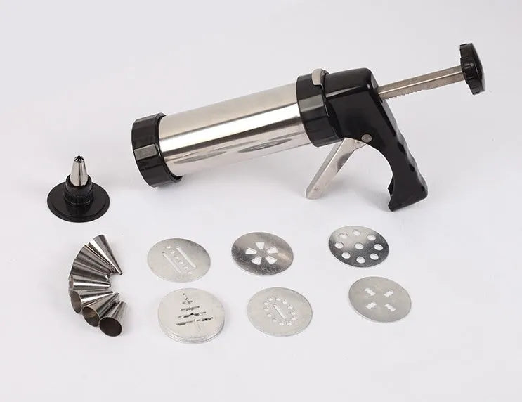 Stainless steel biscuit press gun with assorted cookie mould discs and icing nozzles on a baking tray.