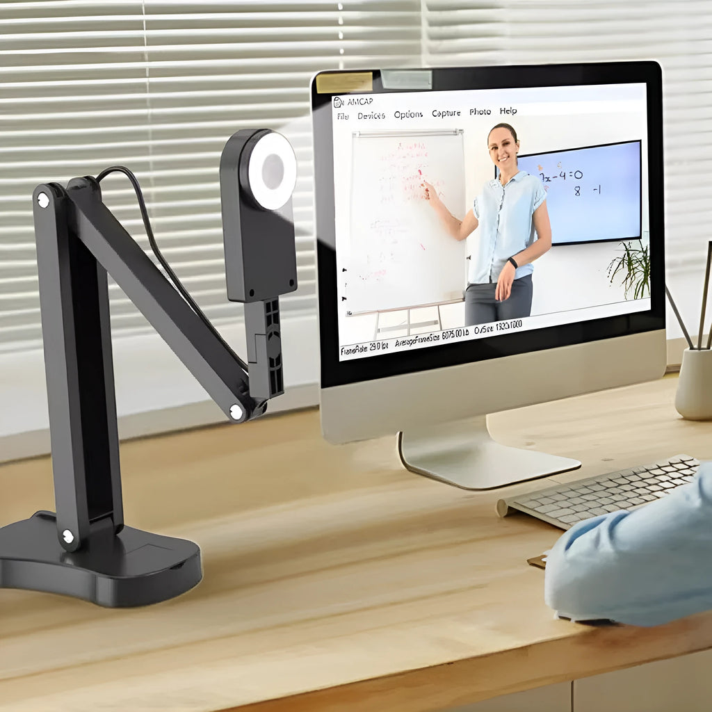 Black USB computer webcam with microphone on a desk, showing its compact design and attached data cable.