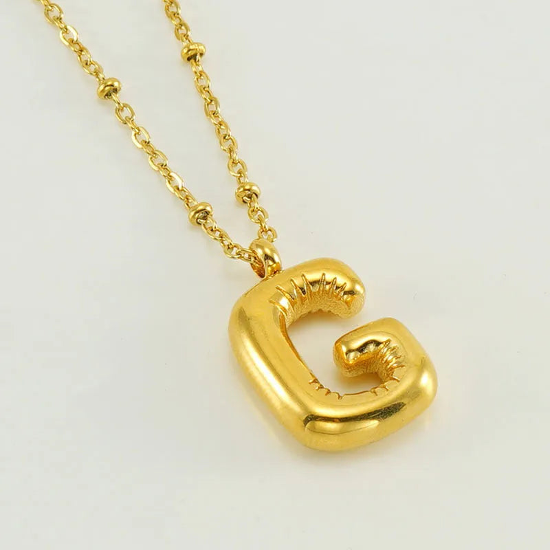Gold bubble letter N pendant on stainless steel clip beads chain necklace against white background