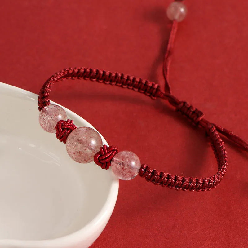 Woven red rope bracelet with a spherical strawberry quartz bead and alloy clasp.