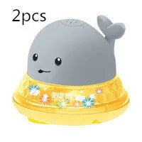 White and blue whale-shaped bath toy spraying water with LED lights on, floating in a baby bath