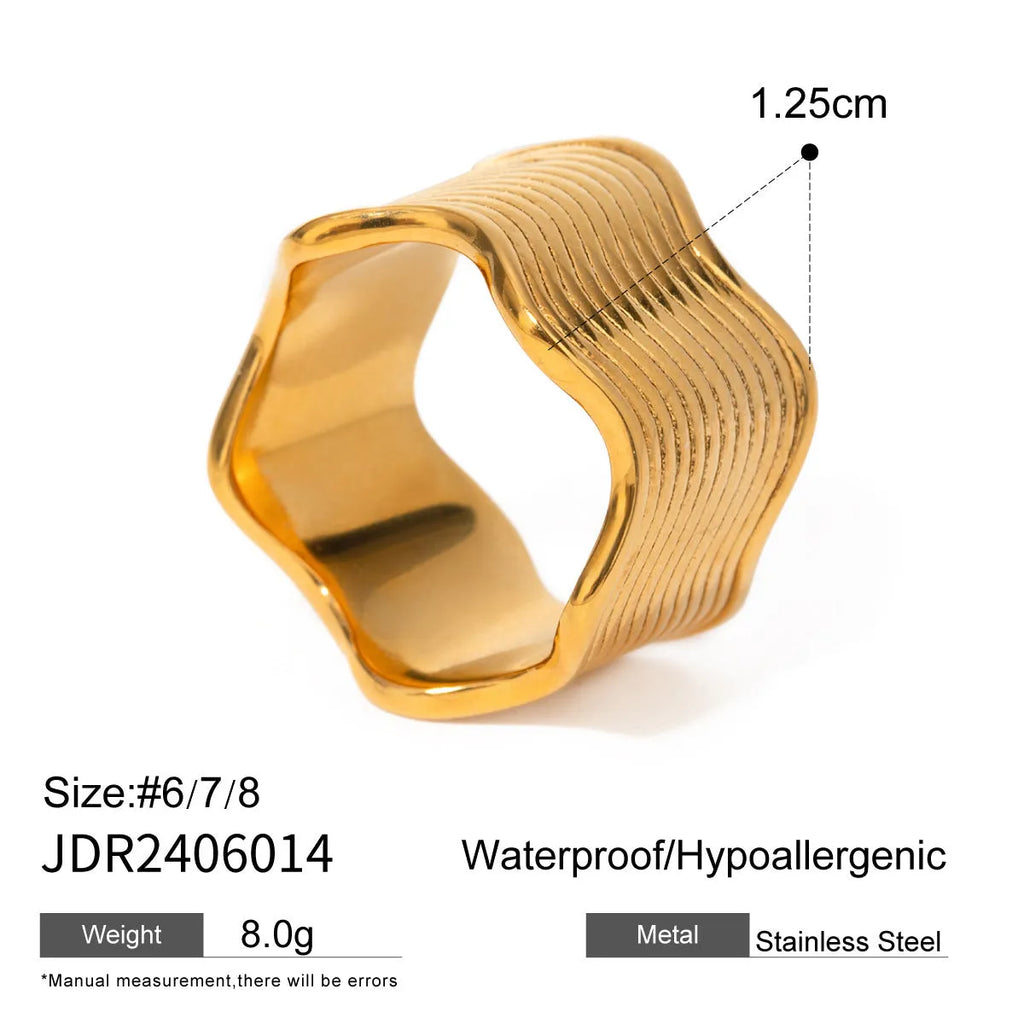 Silver and gold-tone stainless steel ring with a wide geometric wave design on a flat surface.