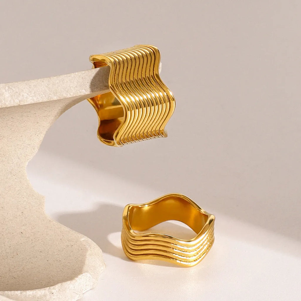 Silver and gold-tone stainless steel ring with a wide geometric wave design on a flat surface.