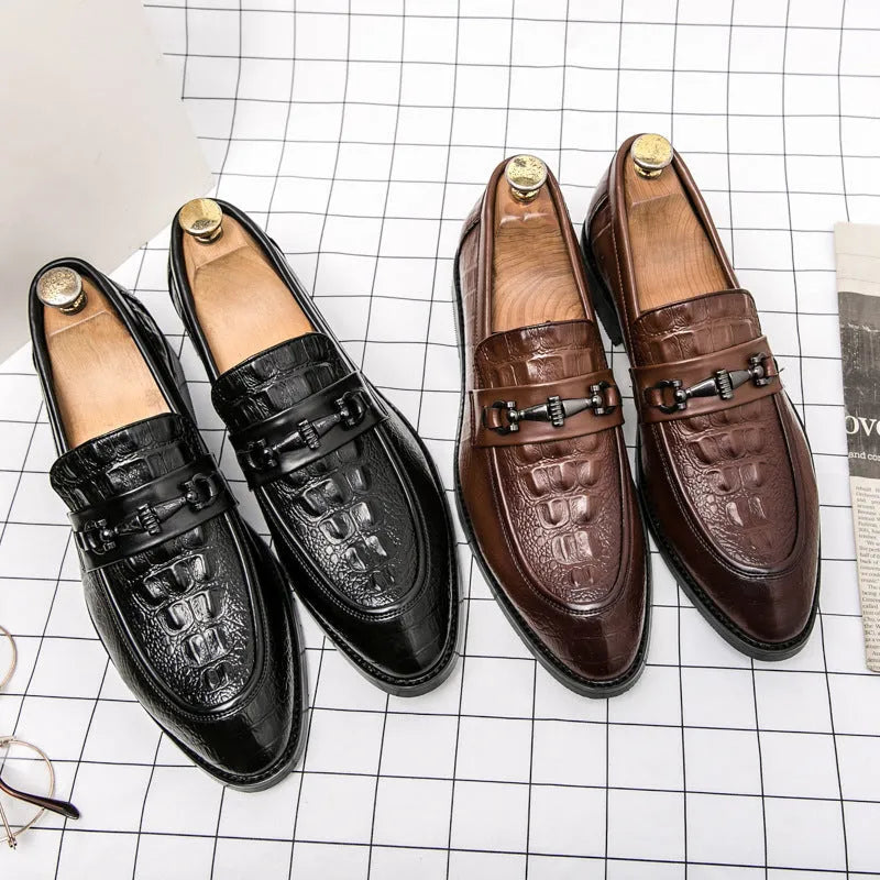 Men's black slip-on formal shoes with pointed toe and belt buckle detail on a light background