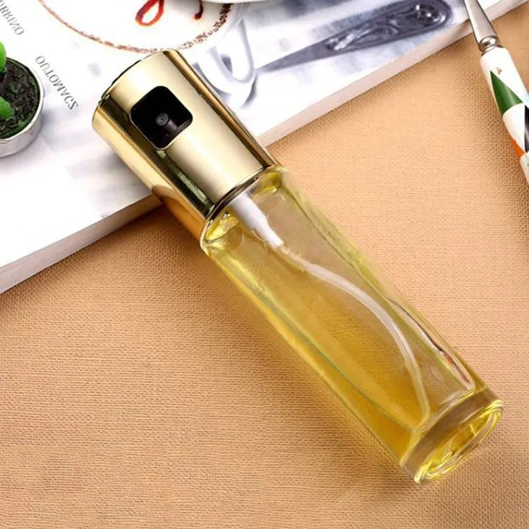 Gold pump-action oil and vinegar spray bottle with 100ml glass body on kitchen counter.