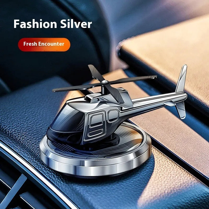 Silver solar-powered rotating metal car air freshener ornament on a dashboard.