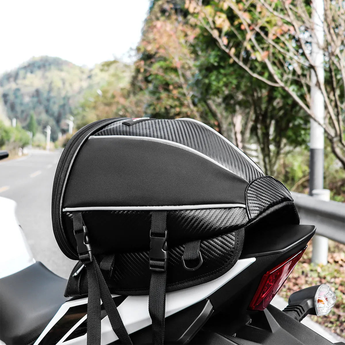 Black motorcycle seat bag with reflective strips, showing multiple pockets and an adjustable shoulder strap.
