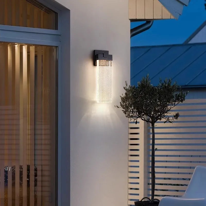 Black stainless steel outdoor LED wall lamp mounted on a wall, showing its rectangular shape and warm light emission.