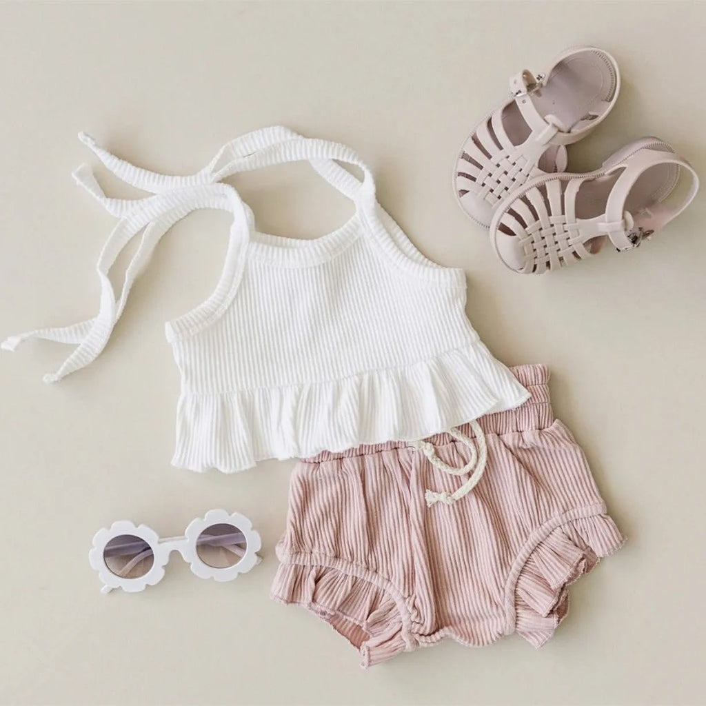 Baby girls white knitted cotton vest and pink shorts set on a light background