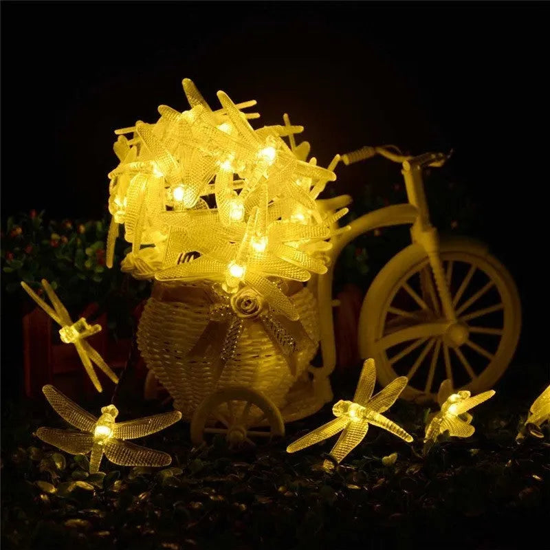 Outdoor solar LED dragonfly string lights with warm white bulbs on a 5-metre cable and a ground-spike solar panel.