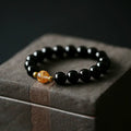 Geometric obsidian and white crystal bracelet with a golden dragon focal bead on a wrist.