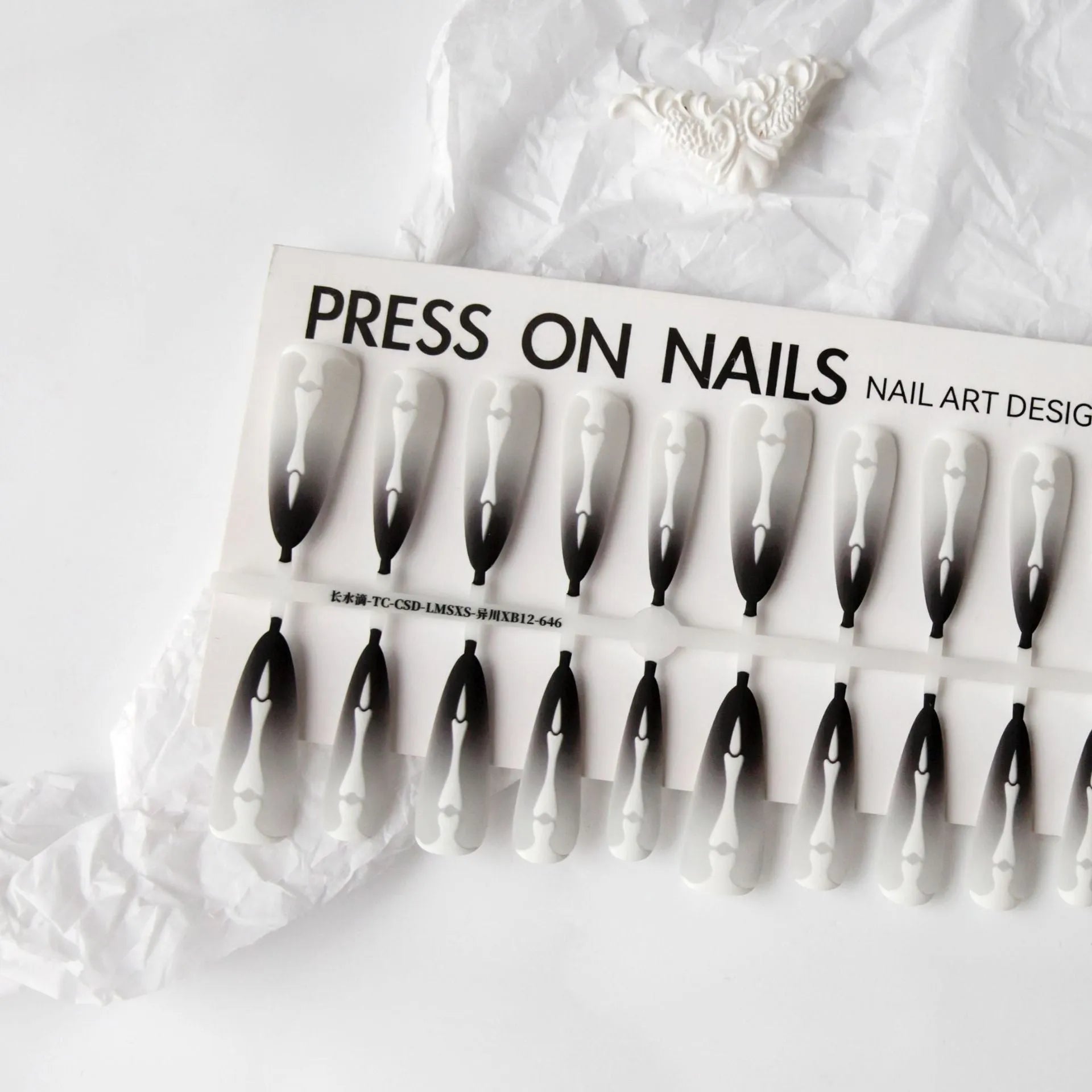 Close-up of long black and pink Christmas gothic nail tips with frosted finish on a flat surface, next to a storage strip.