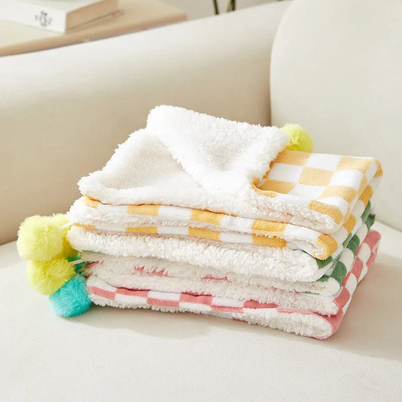 Soft plaid pattern pet blanket with fur ball decoration on a sofa
