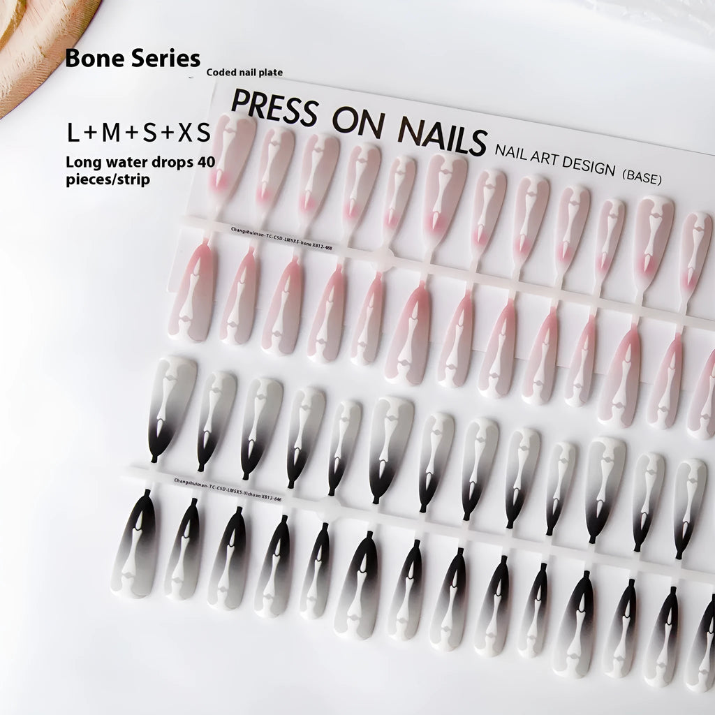 Close-up of long black and pink Christmas gothic nail tips with frosted finish on a flat surface, next to a storage strip.