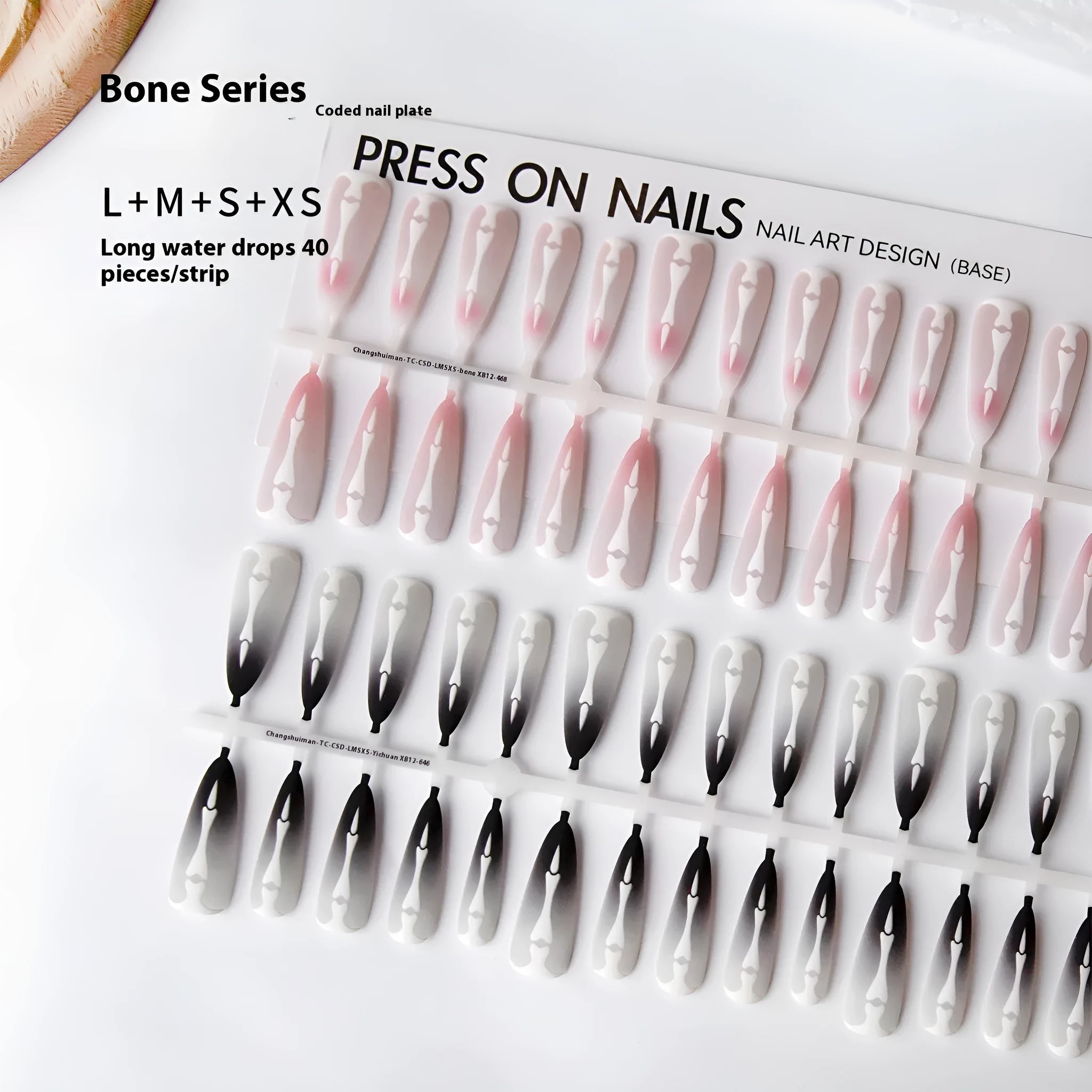 Close-up of long black and pink Christmas gothic nail tips with frosted finish on a flat surface, next to a storage strip.