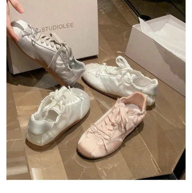 Women's champagne pink satin ballet flats with round toe and lace-up front, shown on a white background.