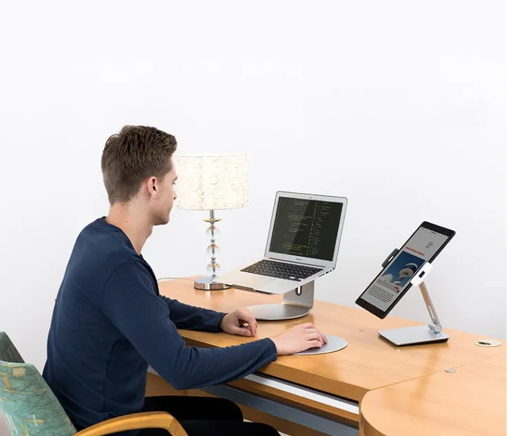 Silver foldable aluminium phone and tablet stand on a desk, holding a tablet at an angle.