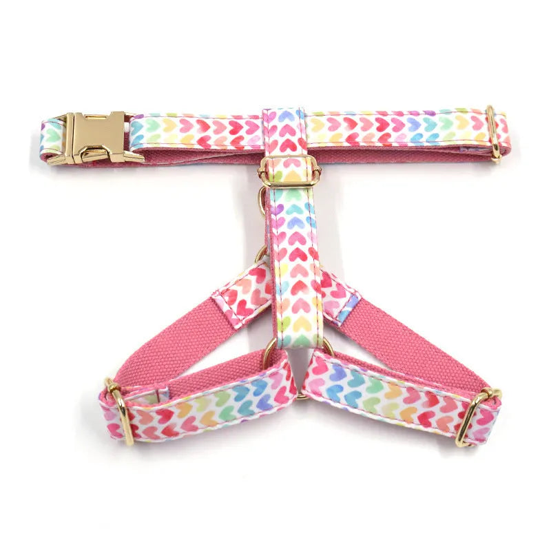 Pink dog harness with a gold buckle and colourful heart-shaped stone decoration on an adjustable polyester strap.