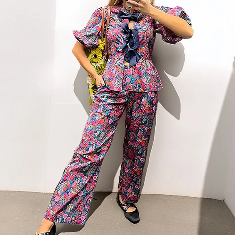 Women's floral print polyester trouser suit with tie-neck top and puff sleeves.