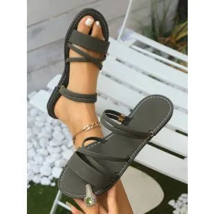 Women's flat sandal with cross strap and flip-toe buckle in black, showing round toe and rubber sole.
